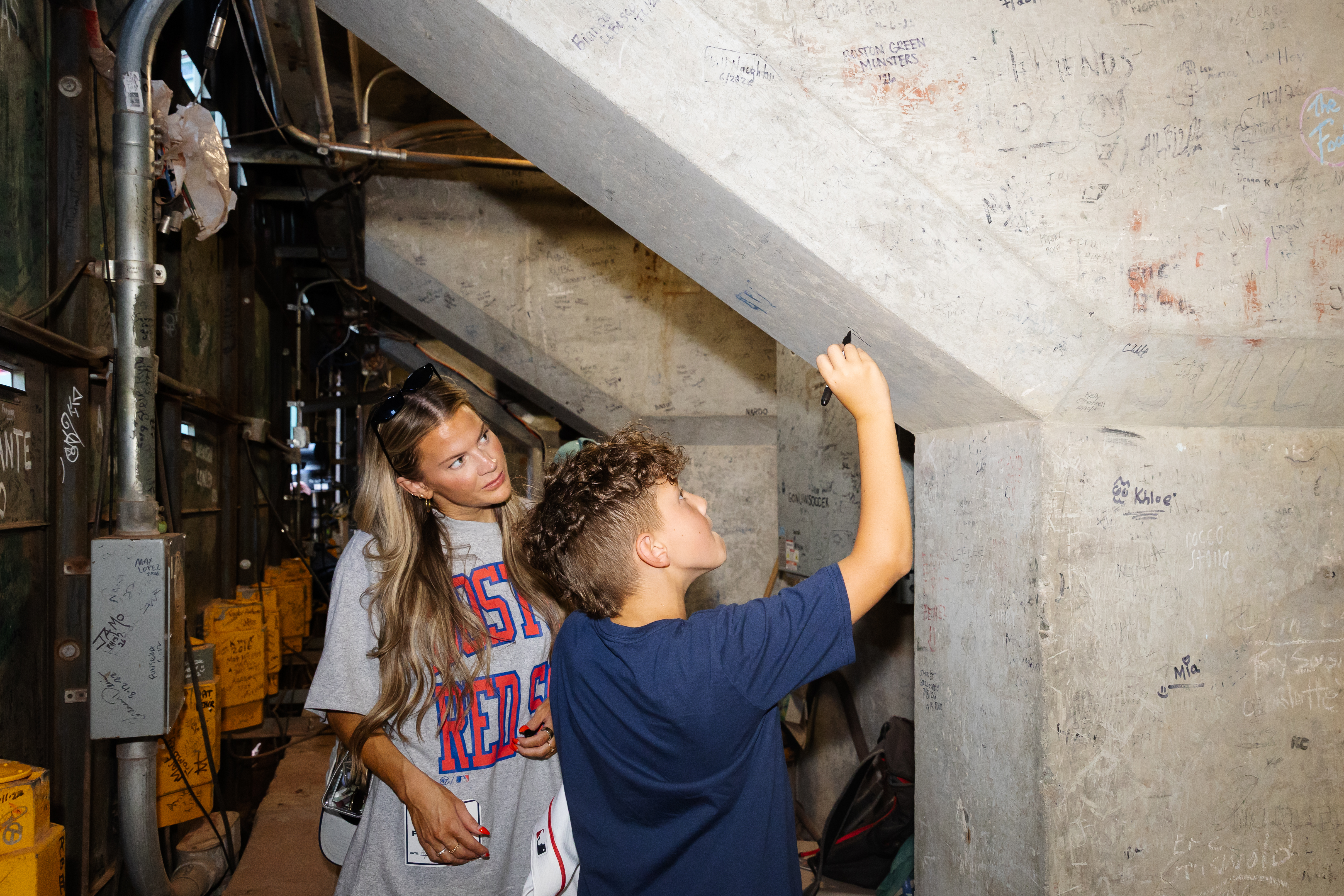 Paxton Glaude signs a support pillar underneath Fenway Park while his mother Abigail looks on. (Photo by Dream On 3)