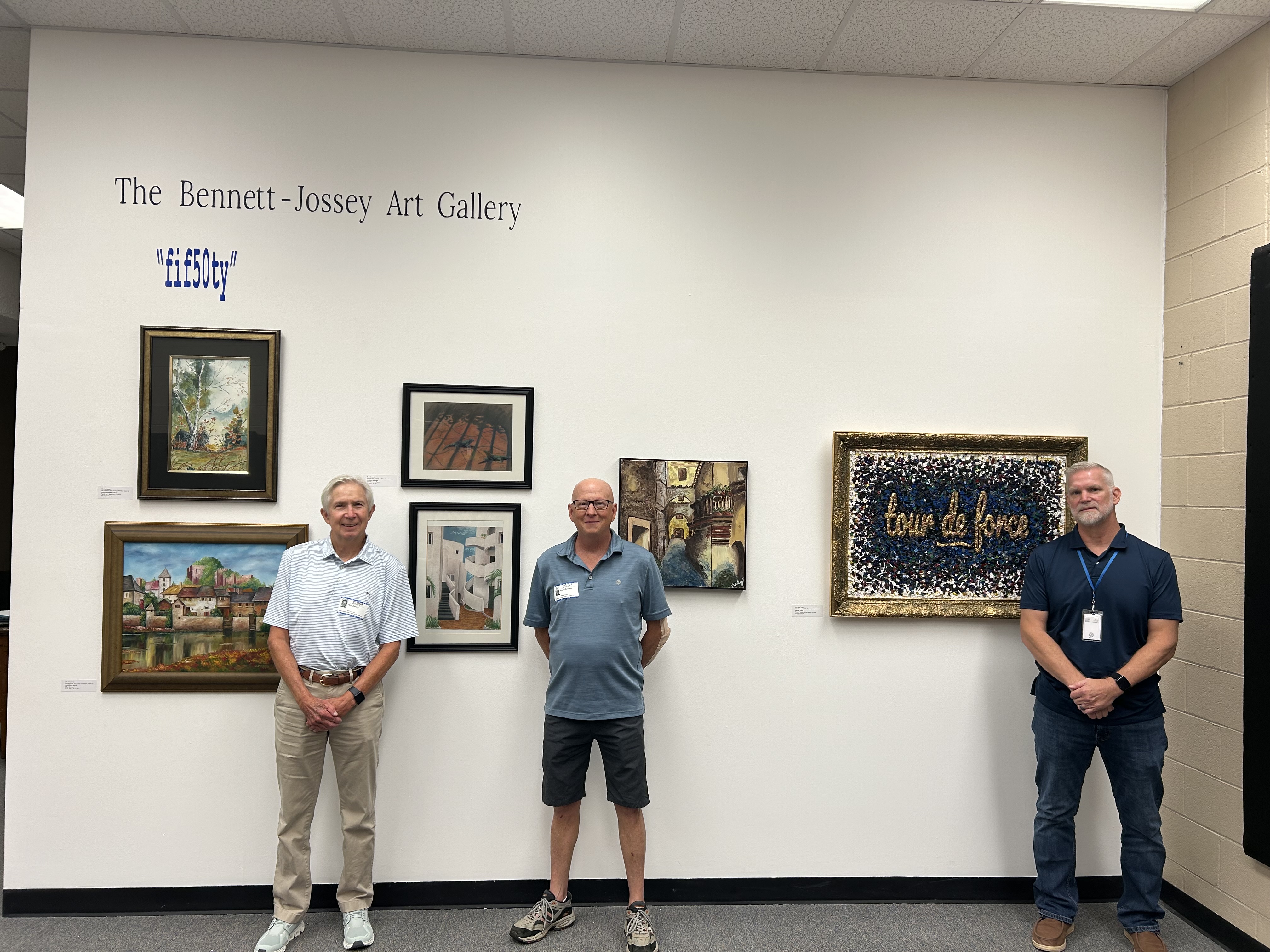Former Elbert County Comprehensive High School art instructors Joe Jossey (left) and David Bennett (middle) pose with current instructor Lee Wells (right) next to an exhibition in the former instructors' honor in the Bennett-Jossey Art Gallery. (Photo by Bo Underwood)