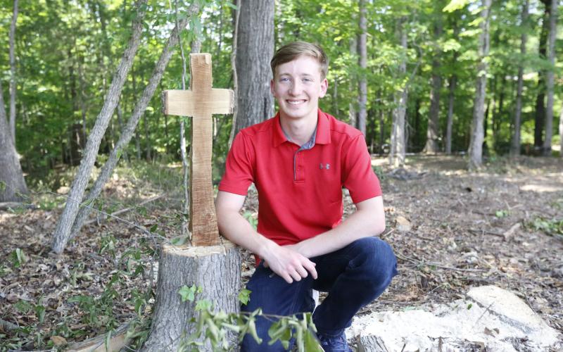 Justin Bastyr, the Valedictorian and STAR Student for the Elbert County Comprehensive School Class of 2021, poses next to the remains of a tree cut into the shape of a cross behind the JROTC building at ECCHS. Bastyr said everything he’s done throughout his high school career has been “for the glory of God.” (Photo by Scoggins)