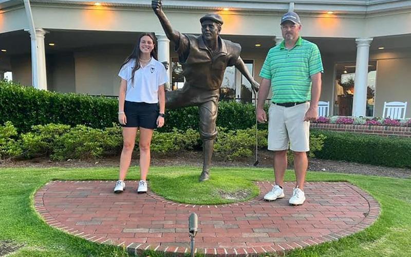 Lady Devil golfer (left) and Devils Head Coach Larry Kesler (right) stand next to a statue of Payne Stewart, the winner of the U.S. Open at Pinehurst No. 2 golf course in 1999.