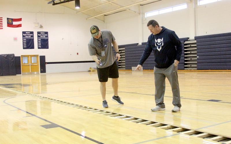 P.E. teachers and coaches (L-R) Drew Greer and Josh Jones examine the gym floor on the teachers’ first day of school after winter break. The floor is still being dried out after being flooded over the holidays.Gym classes are scheduled to be held in the auditorium until the floor is finished. (Photo by Wells)