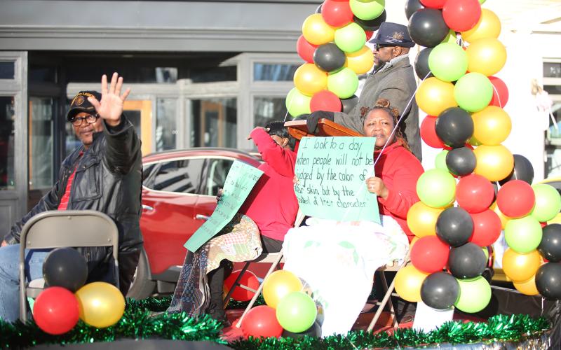 Parade float riders from Vance Creek Baptist Church wave while others hold up signs with quotes from Martin Luther King Jr. (MLK) during the annual MLK. parade Jan. 15. See more photos from the parade and annual Ecumenical Banquet on page 12. (Photo by Wells)