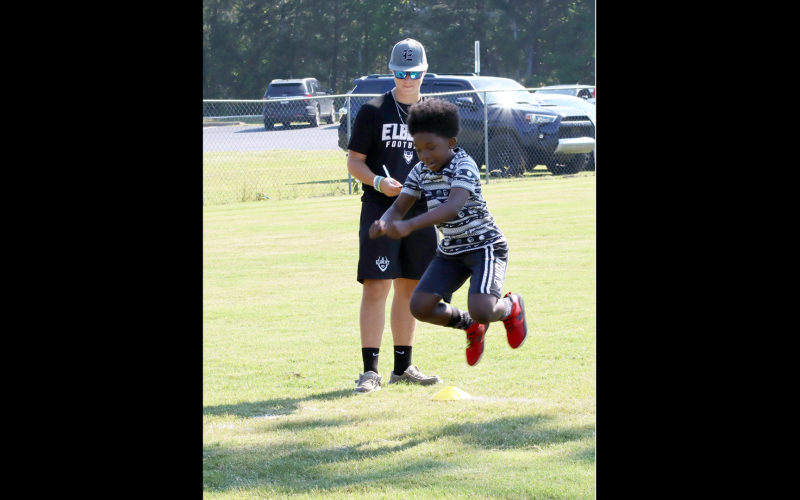 Elbert county fourth grader Lajarvis Heard Jr. propels himself through the air as rising sophomore Braydon Lyon of the ECCHS football program records his jump length.  Lajarvis was one of a couple hundred young people taking part in this year's Friends Helping Friends Club, Inc. Fun Football Day. (Photo by Weeks)