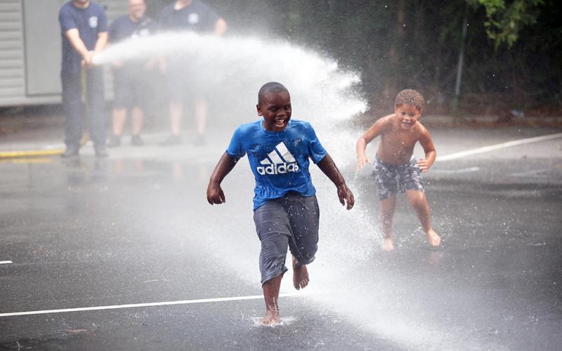 (L-R) Markel Graham and Lawson Childs run through the spray from Elbert County Fire Department's fire truck hose in the parking lot of the library during Big Splash. (Photo by Wells)