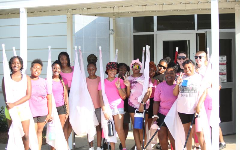 (L-R) Chastity DeJesus, Destiny Patman, Cheslie DeJesus, Ciara Rucker, JerMiriya Perrin, Taniya White, Kemiya Burton, Maurissa Heard, Zaniya Huff, University of Georgia Instructor Addison Kiser, Jimora Brightwell and Color Guard Coach Camilla Long pose for a picture outside the multipurpose room during a break in color guard practice. (Photo by Wells)