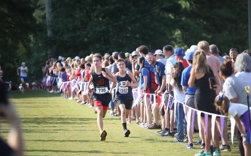 Eli Alexander chases down an opponent at the finish line while his father Evan Alexander (far right, looking), cheers him on during the Northeast Georgia Cross Country Championships. (Photo by Wells)