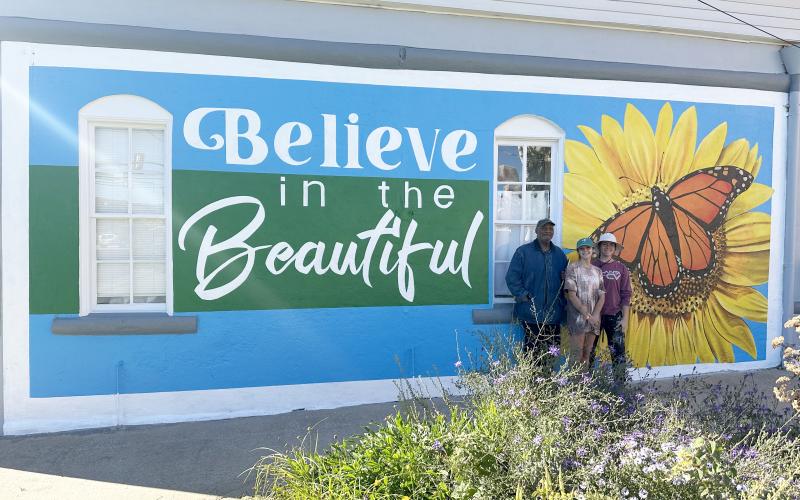 Color the World Bright program director Joseph Norman (left) stands with University of Georgia students Ella Callaro (middle)and Katie Brannen (right) of the Lamar Dodd School of Art in front of the newly-painted mural outside the Keep Elbert County Beautiful office.