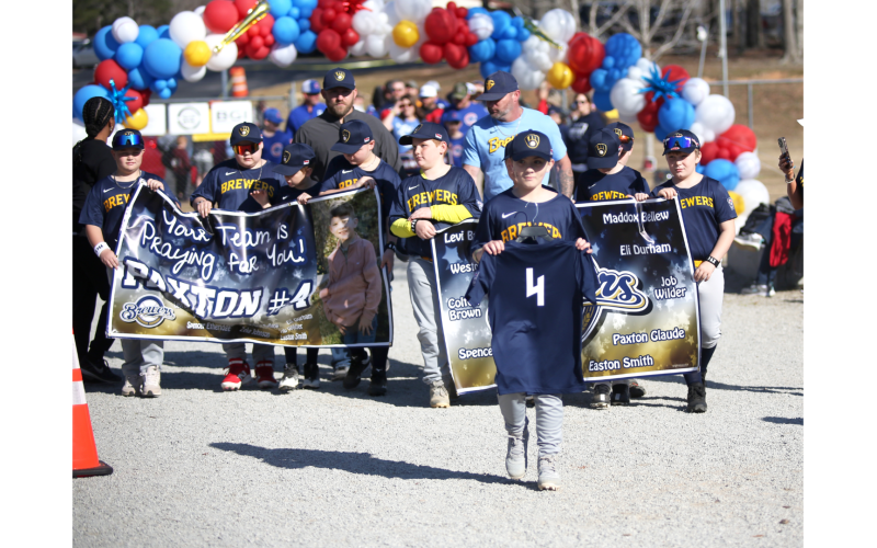The Brewers carried a special sign in honor of their teammate, 9-year-old Paxton Glaude, who was recently seriously injured in a car accident. Carrying his #4 jersey is his cousin, Spencer Ethridge, who was also involved in the accident. (Photo by Wells)