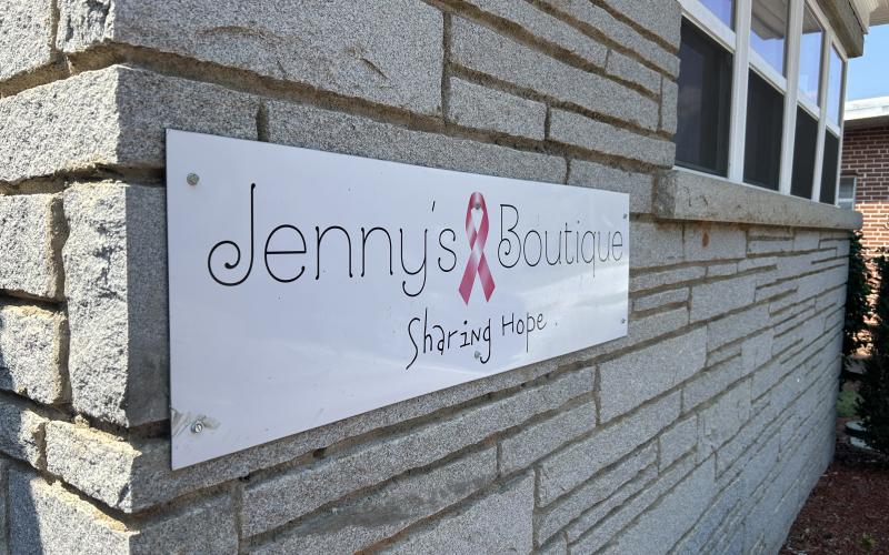 The Jenny's Boutique sign sports a pink ribbon and the phrase "sharing hope." Right, Jenny Jenkins, founder of Jenny's Boutique poses in front of some of the boutique's wig selection. (Photo by Mark Wells)