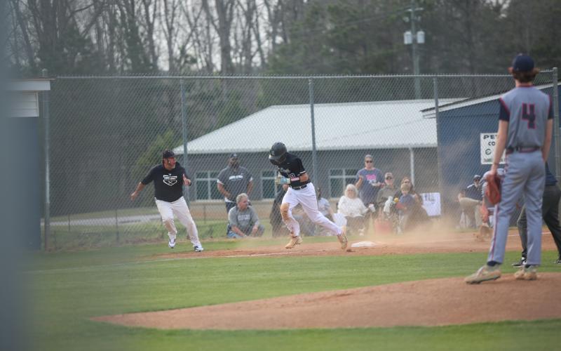 Brody Baker (10) runs home as head coach Lance Ingram coaches him from the third base line.  (Photo by Bo Underwood)