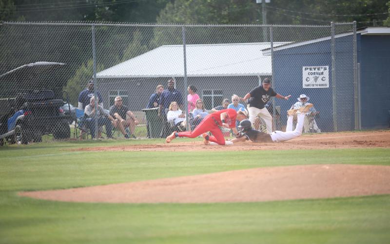 Brody Baker slides into third base as Lance Ingram watches. Elbert County players throw up ‘devil horns’. (Photo by Bo Underwood)
