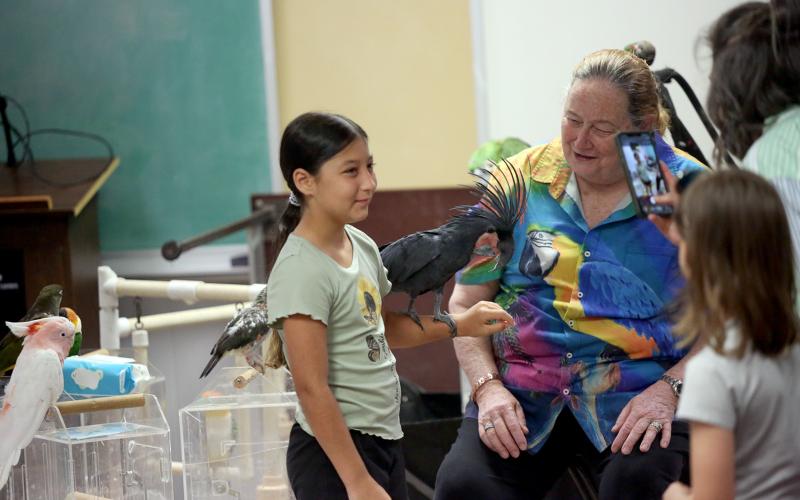 Brenda Bean of Parrot Productions (right) looks on as a child holds one of her birds during a presentation at the Elbert County Public Library. The presentation was part of the library's Summer Reading Program. (Photo by Bo Underwood)