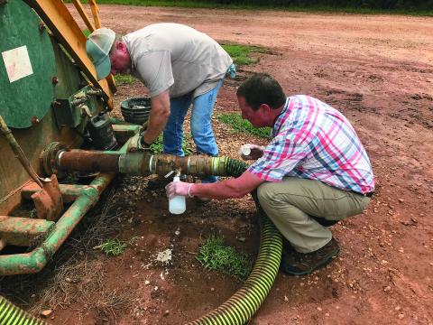 Patrick Marcellino (right) of the University of Georgia’s Elbert County Extension Service and Chad Duffell (left) of Broad River Valley Farms draw fluid from a holding tank in a file photo from 2018 at the River Road facility.  (Photo by Jones)