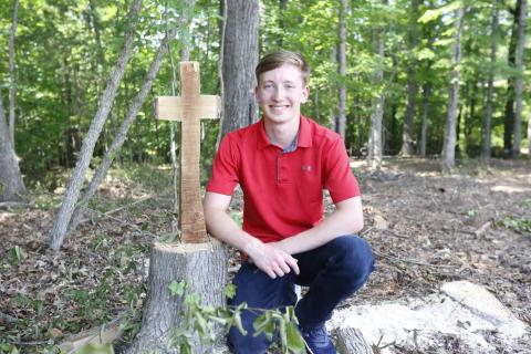 Justin Bastyr, the Valedictorian and STAR Student for the Elbert County Comprehensive School Class of 2021, poses next to the remains of a tree cut into the shape of a cross behind the JROTC building at ECCHS. Bastyr said everything he’s done throughout his high school career has been “for the glory of God.” (Photo by Scoggins)