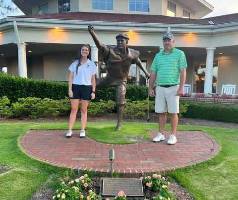 Lady Devil golfer (left) and Devils Head Coach Larry Kesler (right) stand next to a statue of Payne Stewart, the winner of the U.S. Open at Pinehurst No. 2 golf course in 1999.