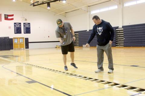 P.E. teachers and coaches (L-R) Drew Greer and Josh Jones examine the gym floor on the teachers’ first day of school after winter break. The floor is still being dried out after being flooded over the holidays.Gym classes are scheduled to be held in the auditorium until the floor is finished. (Photo by Wells)