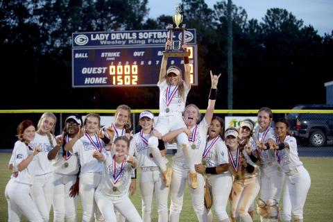 The Lady Devils hold the region championship trophy in front of the scoreboard after defeating Commerce 8-0 at Wesley King Field Oct. 5. (Photo by Wells) 