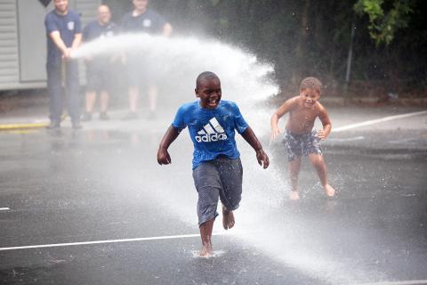(L-R) Markel Graham and Lawson Childs run through the spray from Elbert County Fire Department's fire truck hose in the parking lot of the library during Big Splash. (Photo by Wells)