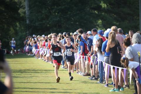 Eli Alexander chases down an opponent at the finish line while his father Evan Alexander (far right, looking), cheers him on during the Northeast Georgia Cross Country Championships. (Photo by Wells)