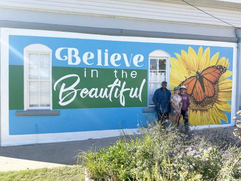 Color the World Bright program director Joseph Norman (left) stands with University of Georgia students Ella Callaro (middle)and Katie Brannen (right) of the Lamar Dodd School of Art in front of the newly-painted mural outside the Keep Elbert County Beautiful office.
