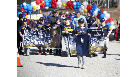 The Brewers carried a special sign in honor of their teammate, 9-year-old Paxton Glaude, who was recently seriously injured in a car accident. Carrying his #4 jersey is his cousin, Spencer Ethridge, who was also involved in the accident. (Photo by Wells)