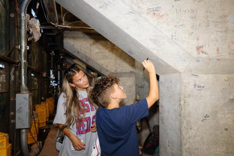 Paxton Glaude signs a support pillar underneath Fenway Park while his mother Abigail looks on. (Photo by Dream On 3)
