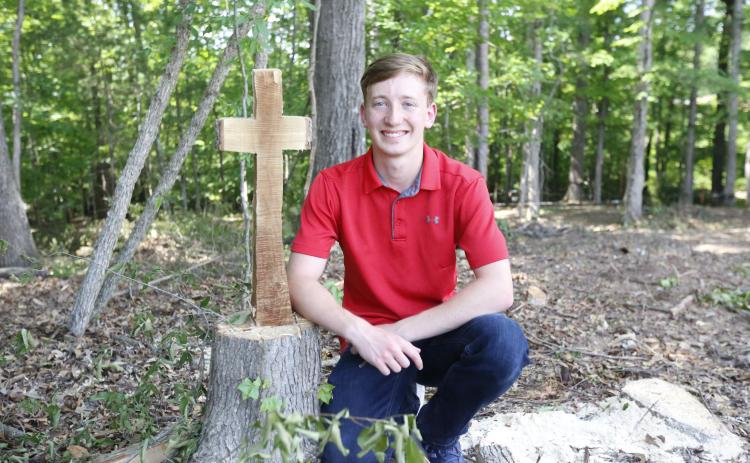 Justin Bastyr, the Valedictorian and STAR Student for the Elbert County Comprehensive School Class of 2021, poses next to the remains of a tree cut into the shape of a cross behind the JROTC building at ECCHS. Bastyr said everything he’s done throughout his high school career has been “for the glory of God.” (Photo by Scoggins)