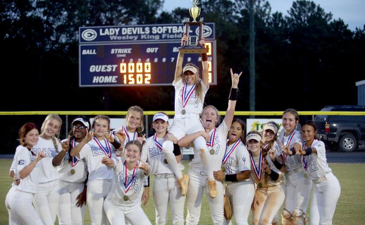 The Lady Devils hold the region championship trophy in front of the scoreboard after defeating Commerce 8-0 at Wesley King Field Oct. 5. (Photo by Wells)