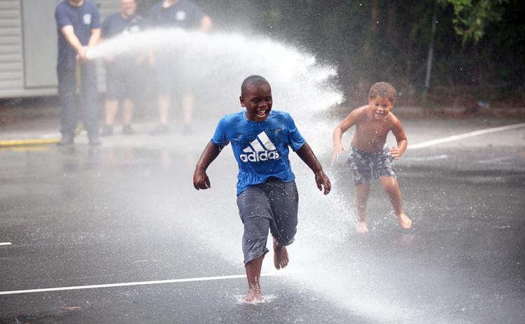 (L-R) Markel Graham and Lawson Childs run through the spray from Elbert County Fire Department's fire truck hose in the parking lot of the library during Big Splash. (Photo by Wells)
