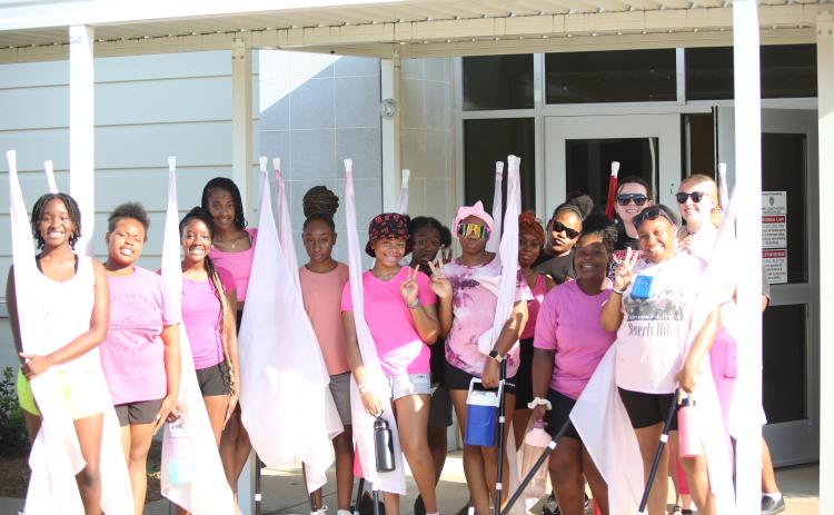(L-R) Chastity DeJesus, Destiny Patman, Cheslie DeJesus, Ciara Rucker, JerMiriya Perrin, Taniya White, Kemiya Burton, Maurissa Heard, Zaniya Huff, University of Georgia Instructor Addison Kiser, Jimora Brightwell and Color Guard Coach Camilla Long pose for a picture outside the multipurpose room during a break in color guard practice. (Photo by Wells)