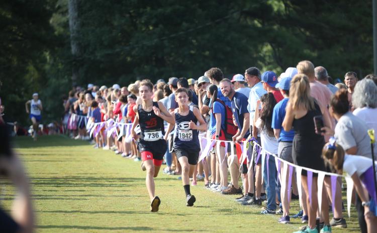 Eli Alexander chases down an opponent at the finish line while his father Evan Alexander (far right, looking), cheers him on during the Northeast Georgia Cross Country Championships. (Photo by Wells)