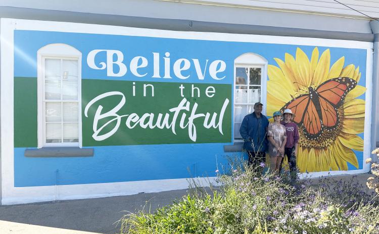 Color the World Bright program director Joseph Norman (left) stands with University of Georgia students Ella Callaro (middle)and Katie Brannen (right) of the Lamar Dodd School of Art in front of the newly-painted mural outside the Keep Elbert County Beautiful office.