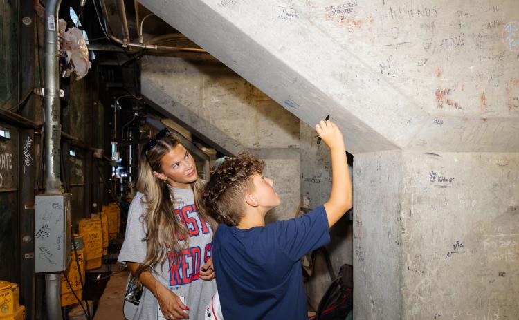 Paxton Glaude signs a support pillar underneath Fenway Park while his mother Abigail looks on. (Photo by Dream On 3)