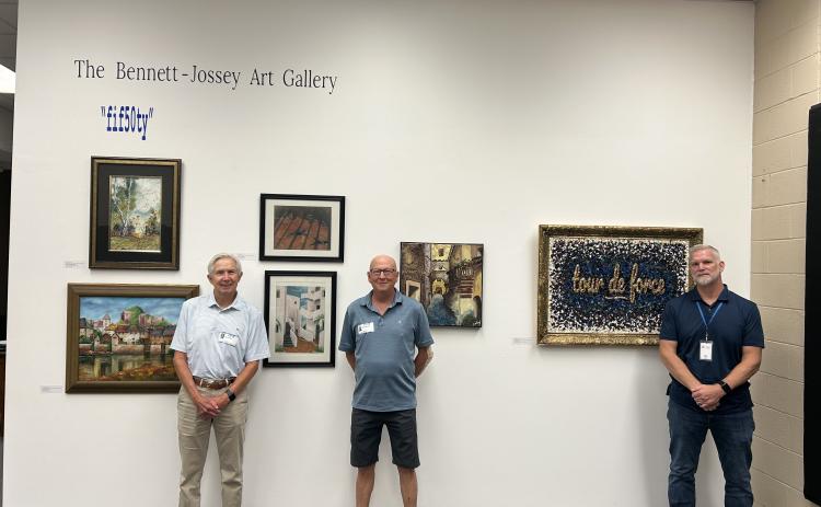 Former Elbert County Comprehensive High School art instructors Joe Jossey (left) and David Bennett (middle) pose with current instructor Lee Wells (right) next to an exhibition in the former instructors' honor in the Bennett-Jossey Art Gallery. (Photo by Bo Underwood)