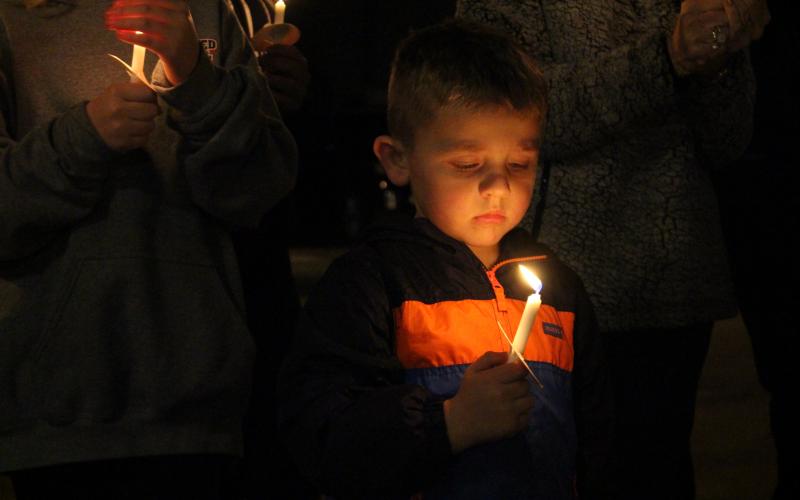 A candlelight vigil was held during a bench dedication in honor of James F. Creason at Friday’s Christmas Caroling Event in Bowman, and the candle shines here on Creason’s great-grandson, Easton Moss. (Photo by Scoggins) 