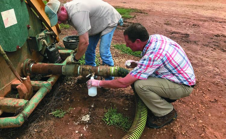 Patrick Marcellino (right) of the University of Georgia’s Elbert County Extension Service and Chad Duffell (left) of Broad River Valley Farms draw fluid from a holding tank in a file photo from 2018 at the River Road facility.  (Photo by Jones)