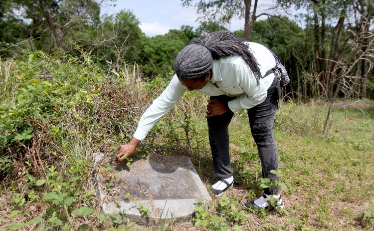 Jim-Ree Museum co-founder and owner Aurolyn White brushes off vegetation from a fallen over headstone at the back of Pinetown Cemetery near Second Street Extension. Through memories and passed down stories, White and others in the area believe there could be graves of African Americans on property located on the opposite side of the street from the cemetery. (Photo by Scoggins)